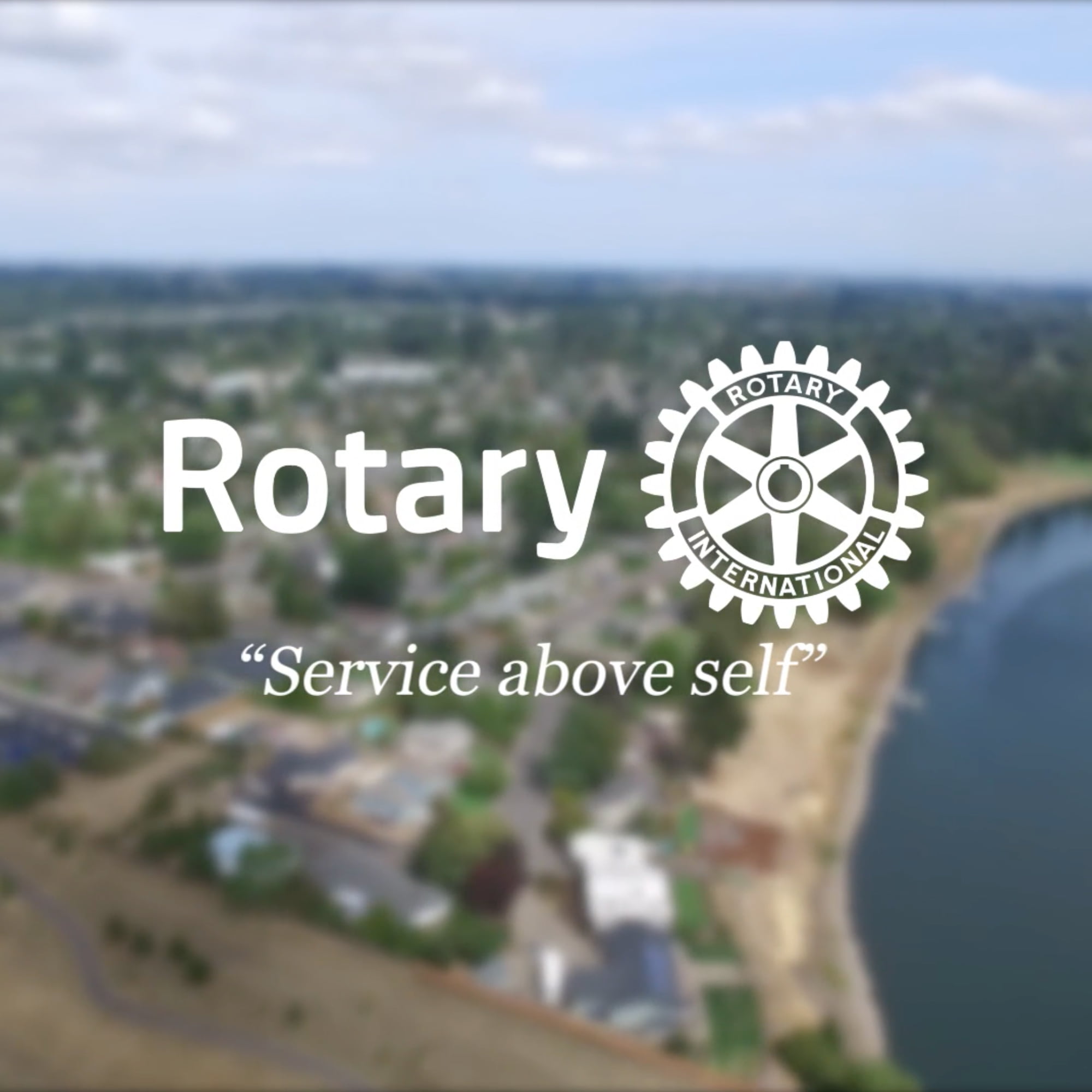 Blurred out aerial view of river and town with Rotary logo and "service above self" overlaid